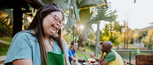 A person with disability wearing an apron serves patrons in an outdoor cafe